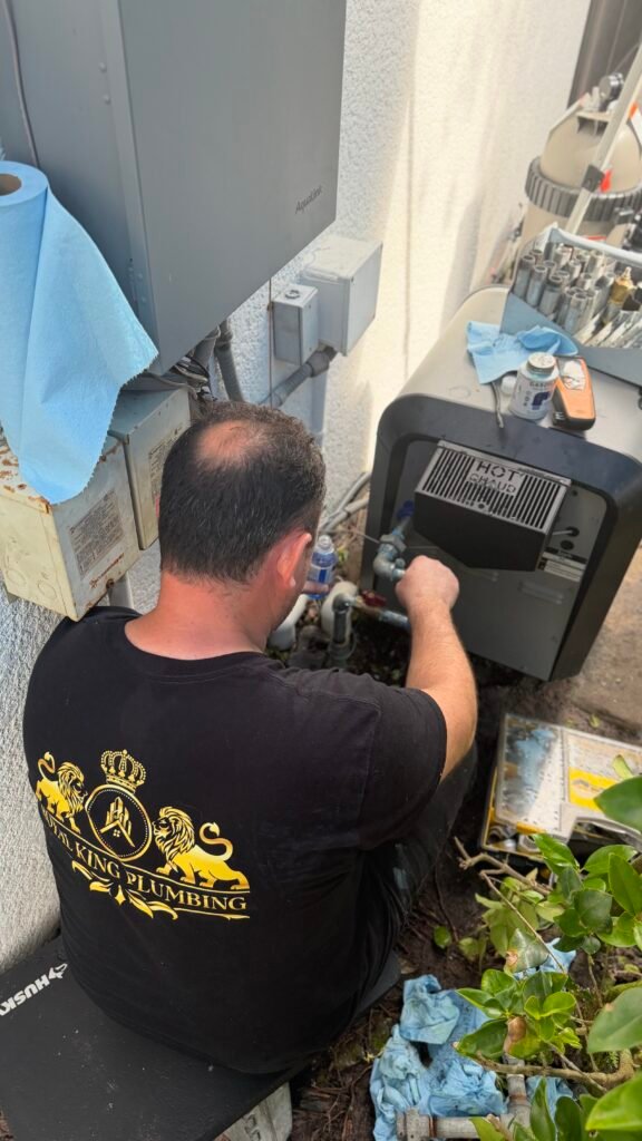 A Royal King Plumbing technician in the original company-logo shirt working beside outdoor pool equipment.